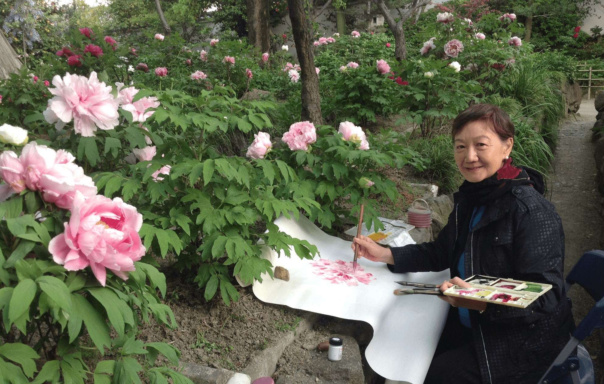 Artist painting pink peonies in garden